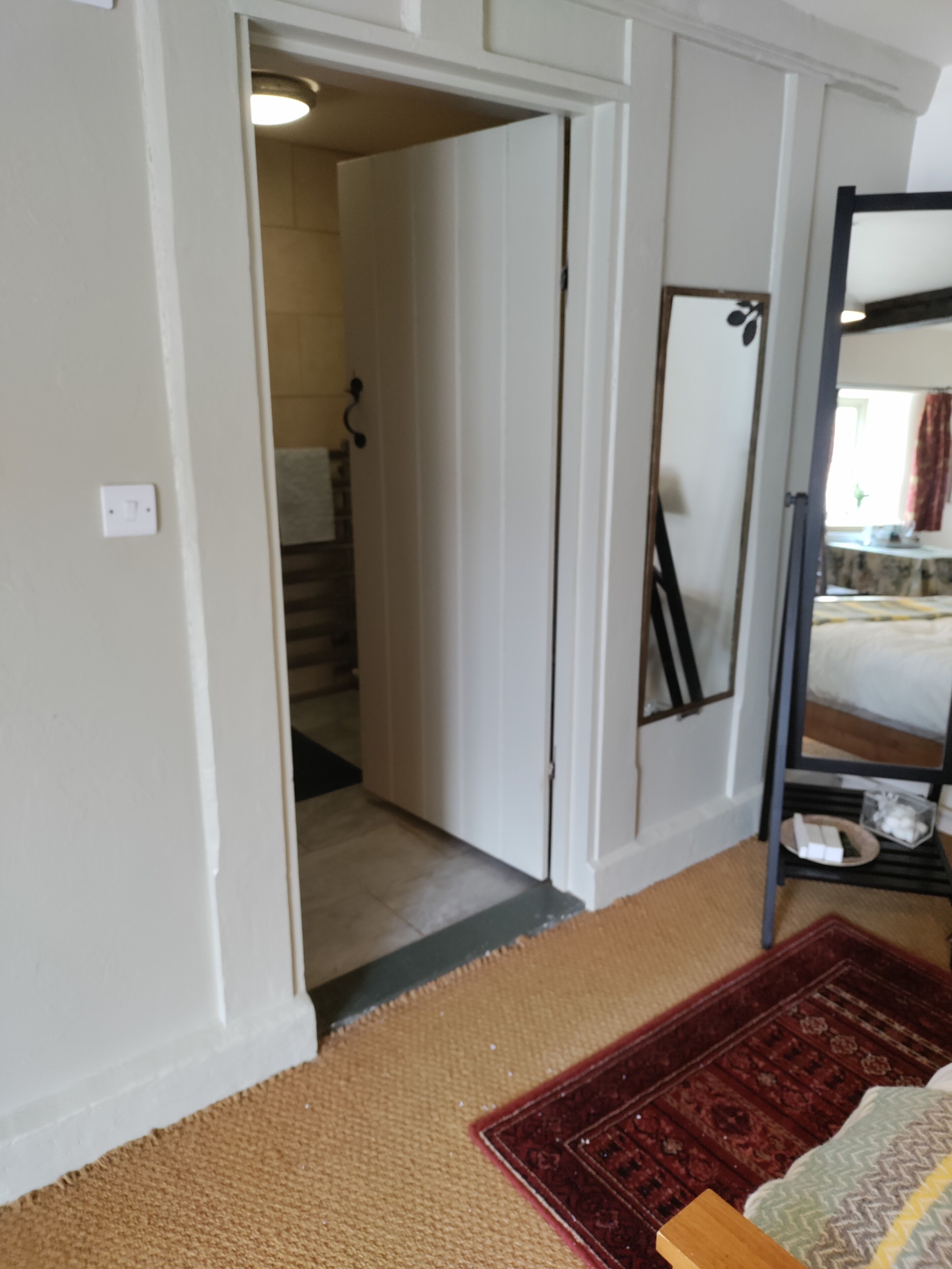 A room with a bed, a mirror, a shelf with toiletries, and a door leading to a bathroom.