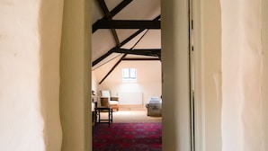 A narrow hallway with exposed wooden beams, leading to a room with a red carpet and a window. - Lower Severalls Farmhouse (Crewkerne)