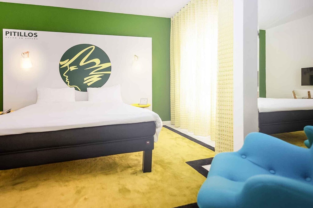 Una habitación de hotel con cama, pared de acento verde, un logotipo grande y una silla azul.