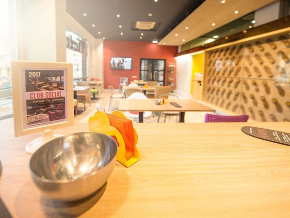 A restaurant interior with a dining area, a TV screen, and a poster advertising a social club event. - ibis Styles La Rioja Arnedo (Arnedo)