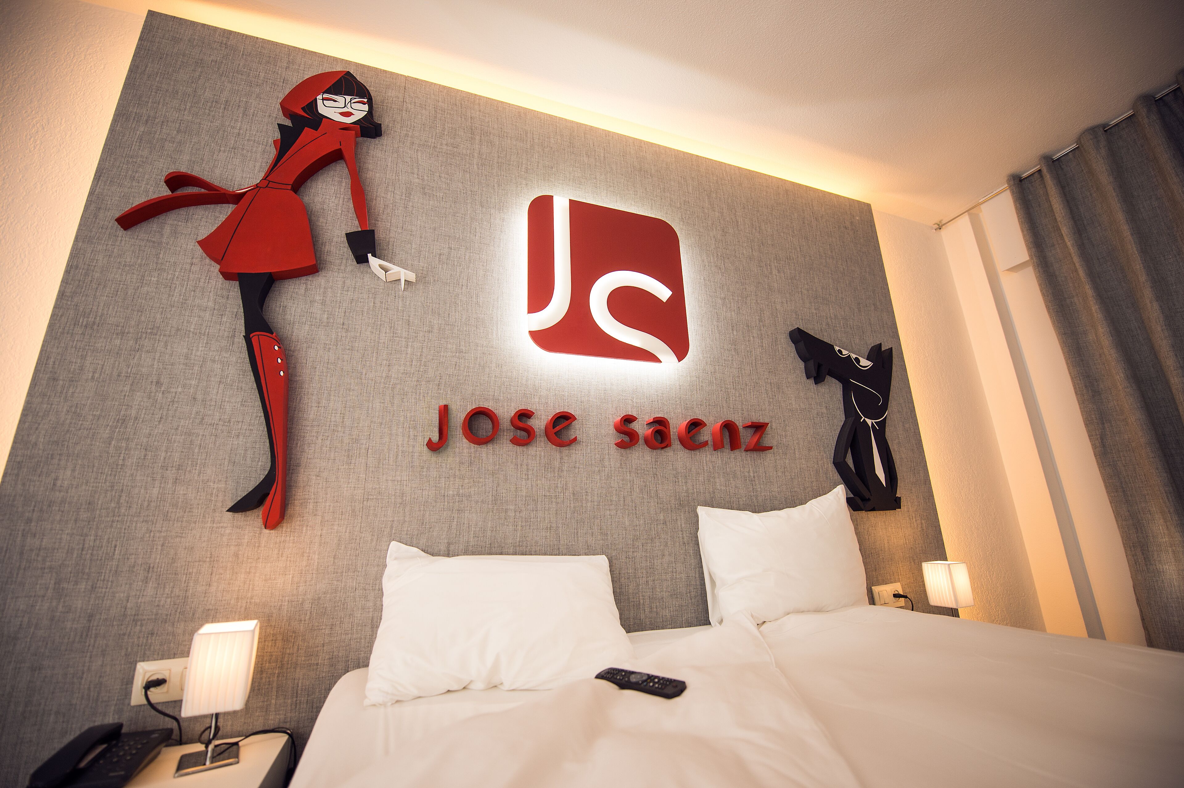 Een hotelkamer met een bed, nachtkastje, lamp en een decoratie aan de muur.