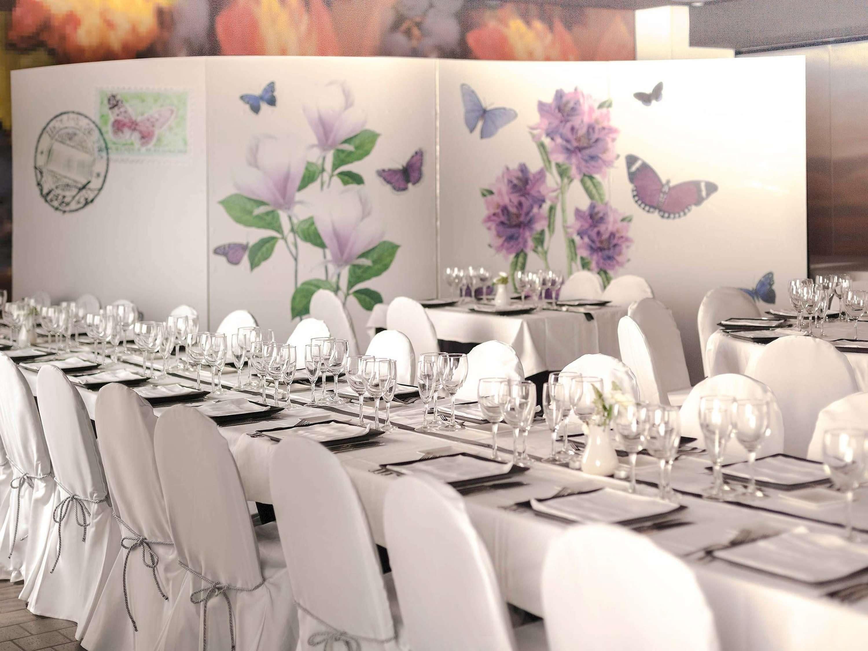 Een balzaal met lange tafels gedekt voor een formeel evenement, inclusief witte stoelen en servies.