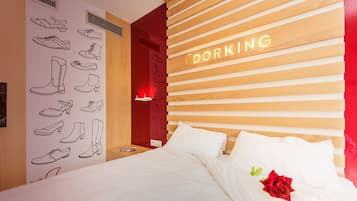 A hotel room with a bed, a wall with shoe illustrations, and a neon sign that reads "DORKING".