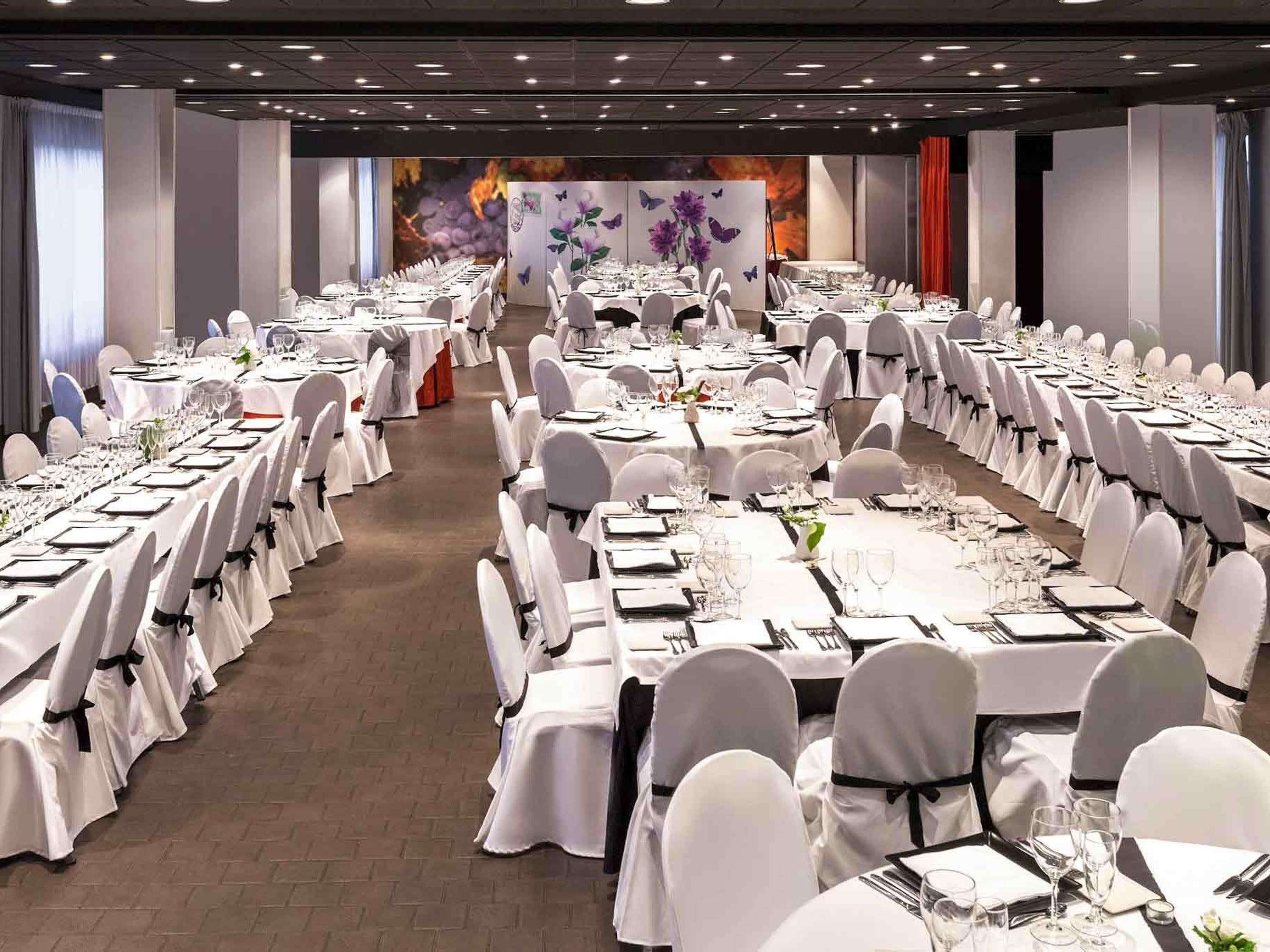 A banquet hall with round tables set for dining, white chairs, and a stage with floral decorations.