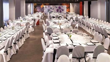 A banquet hall with round tables set for dining, white chairs, and a stage with floral decorations.
