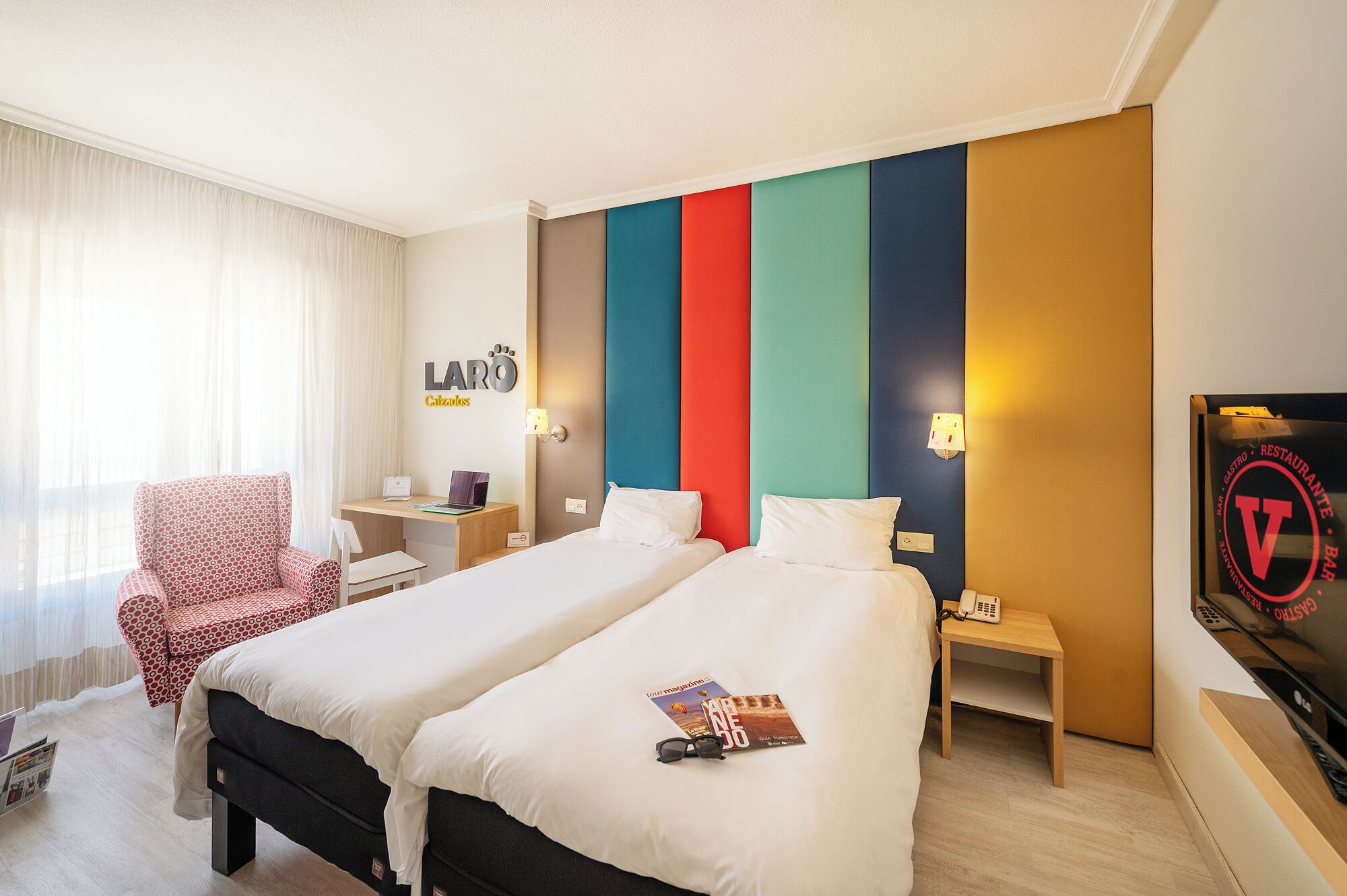A hotel room with two beds, a desk, a chair, and a TV.