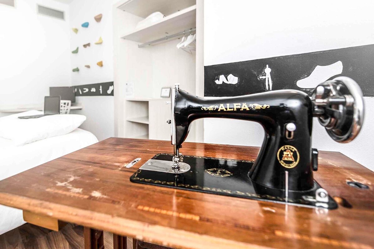 A sewing machine on a wooden table in a room with white walls and shelves.