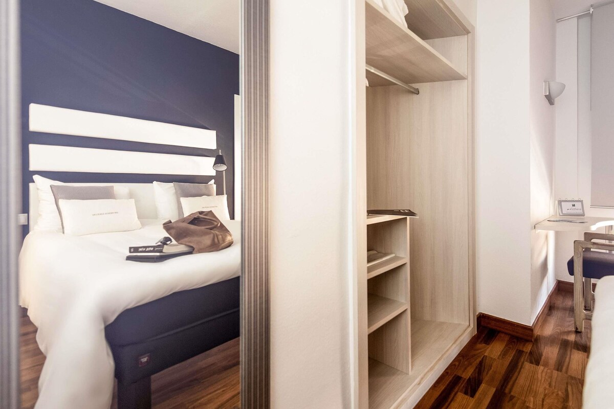 A hotel room with a bed, bedside table, and a wardrobe.