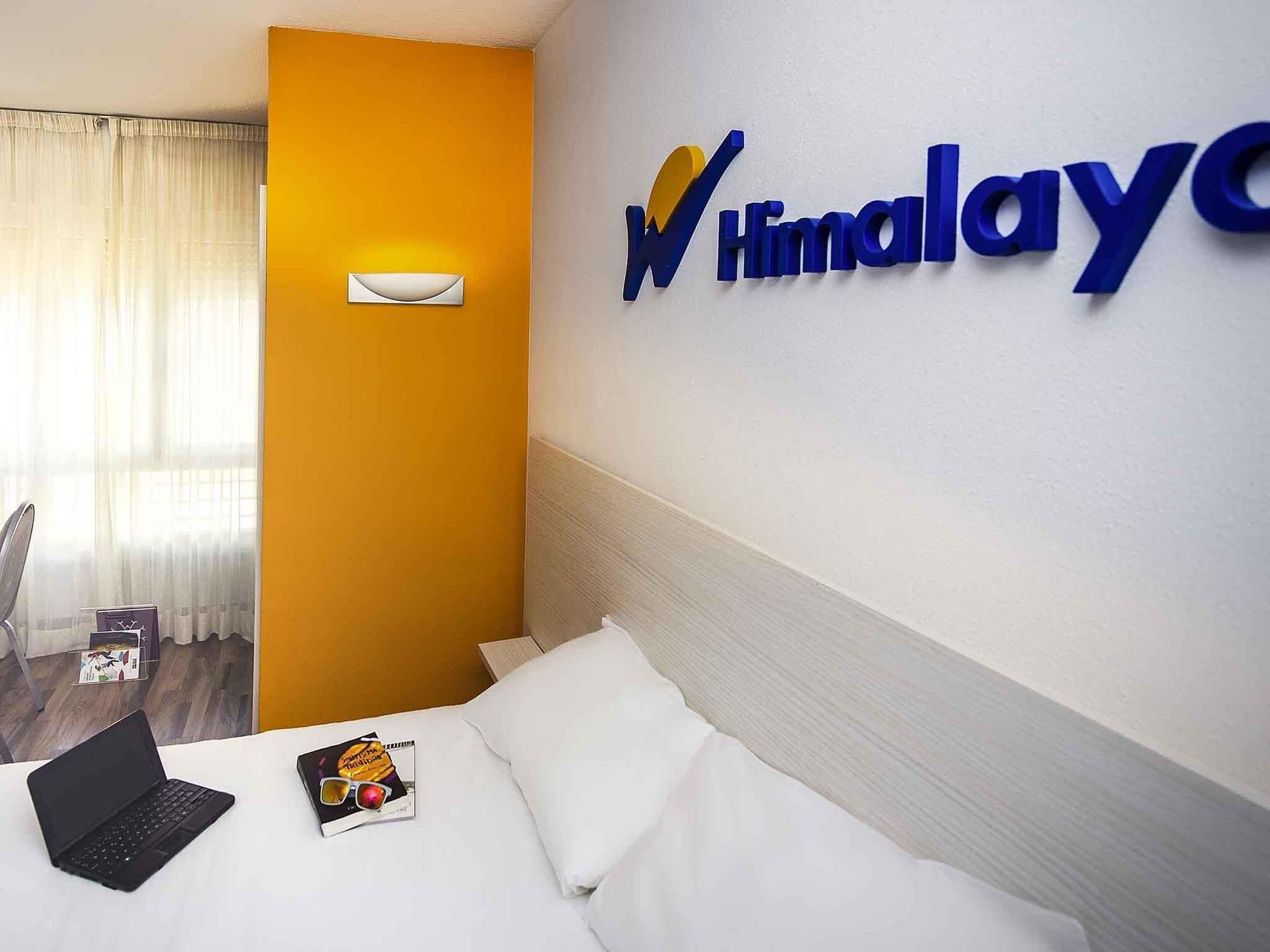A hotel room with a bed, a laptop, sunglasses, and a magazine on the bed. There is a wall-mounted sign with the hotel's name.
