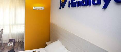 A hotel room with a bed, a laptop, sunglasses, and a magazine on the bed. There is a wall-mounted sign with the hotel's name.