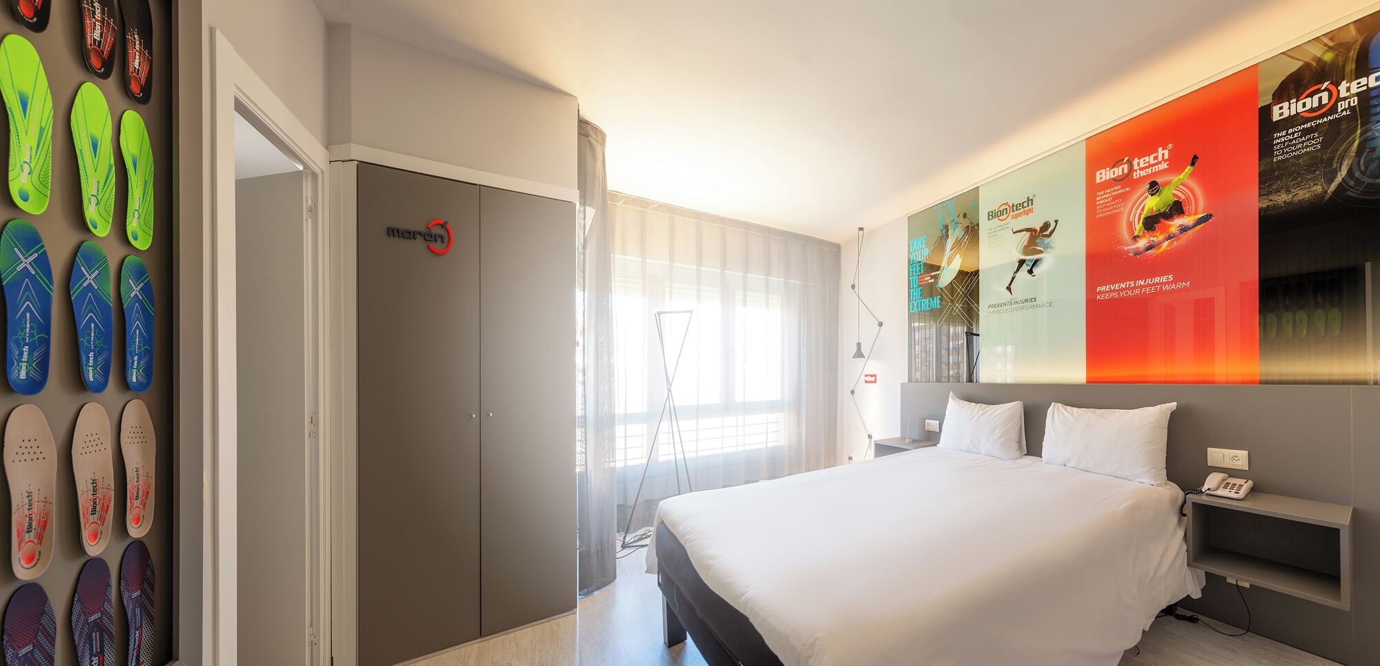 A hotel room with a bed, a wardrobe, and a wall with flip-flops.