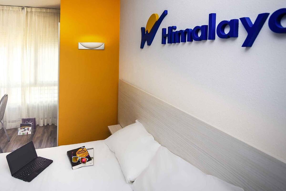 A hotel room with a bed, a laptop, and a magazine on the bed. There is a wall-mounted sign with the hotel name.