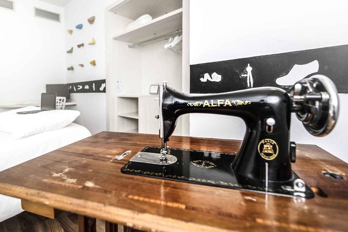 A sewing machine on a wooden table in a room with white walls and shelves.