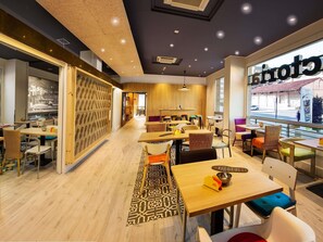 Interior moderno de restaurante con suelo de madera, diversas opciones de asientos y vistas a la calle a través de grandes ventanales.