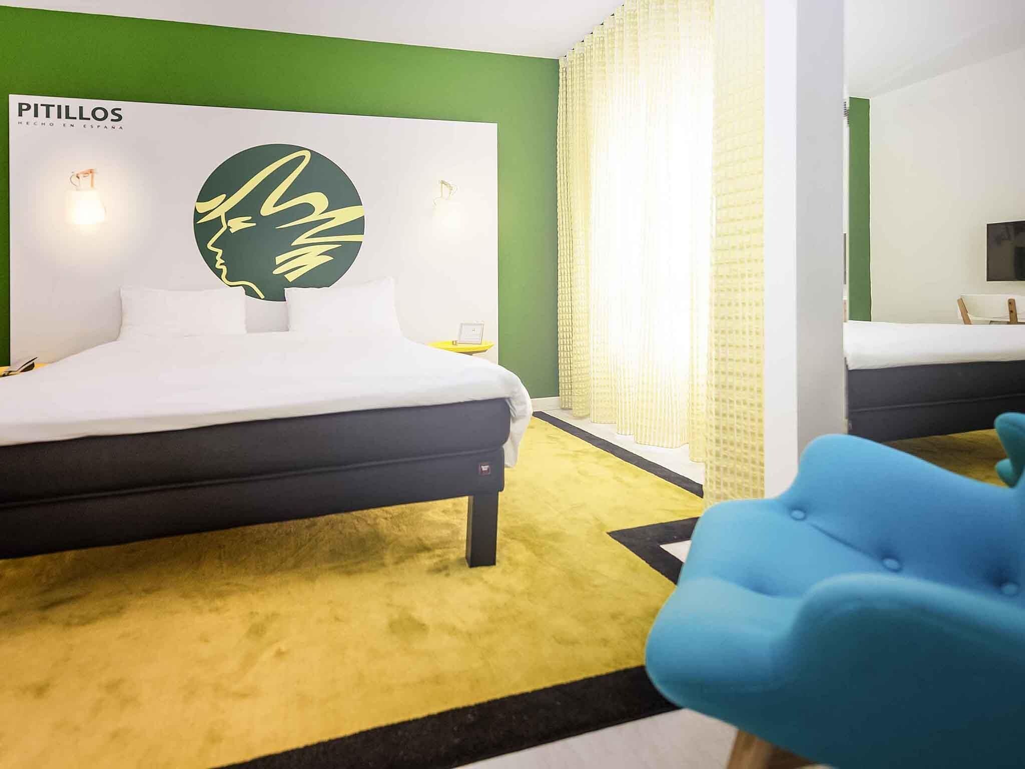 Una habitación de hotel con cama, pared de acento verde, un logotipo grande y una silla azul.