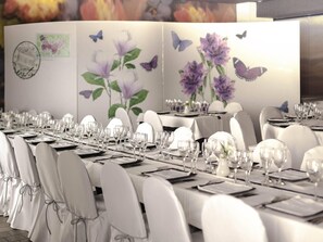 A long dining table set with white chairs, glasses, and plates, with floral wall art and a butterfly motif. - ibis Styles La Rioja Arnedo (Arnedo)