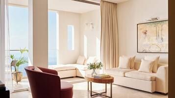 Een moderne woonkamer met een rode fauteuil, een beige bank en een salontafel. Een groot raam zorgt voor daglicht en uitzicht op het landschap.