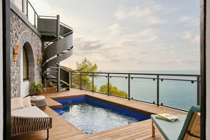 A modern outdoor swimming pool with a wooden deck, a spiral staircase, and a view of the sea.