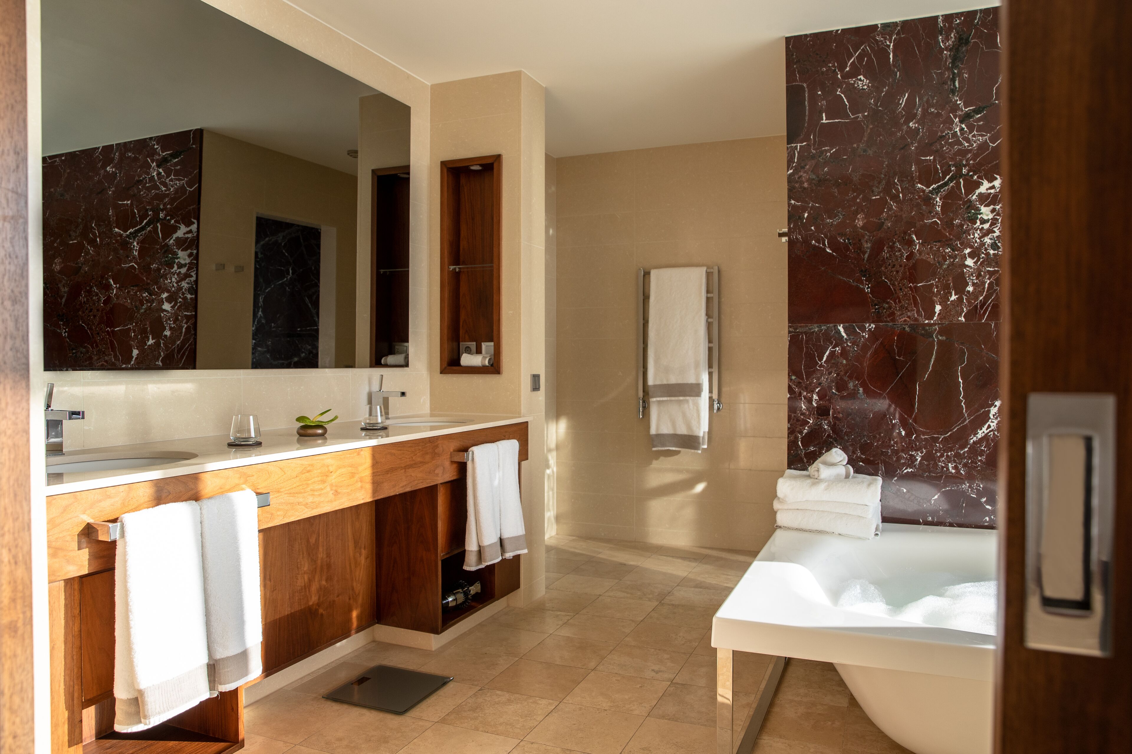 A modern bathroom with a marble vanity, a large mirror, a bathtub, and a towel rack.