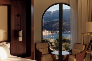 A hotel room with a large arched window, two armchairs, a small round table, and a bed. - Jumeirah Mallorca (Sóller)