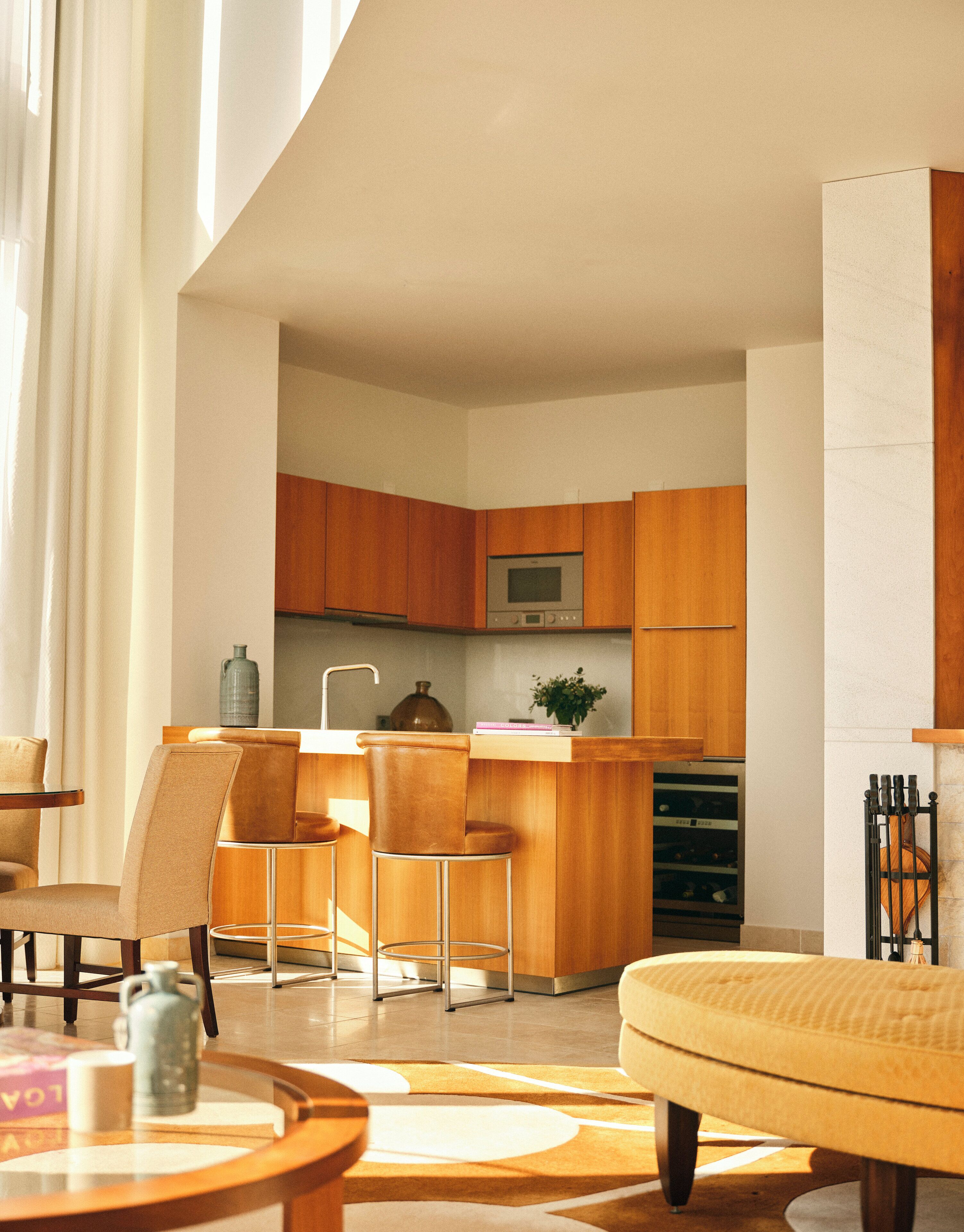 Een moderne keuken met houten kastjes, een centraal eiland en een inbouwoven. Er is een eethoek met een ronde tafel en stoelen, en een bank.