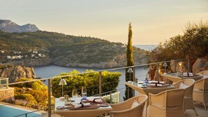 Una terraza con mobiliario de mimbre, una piscina y una vista panorámica de un lago y montañas.