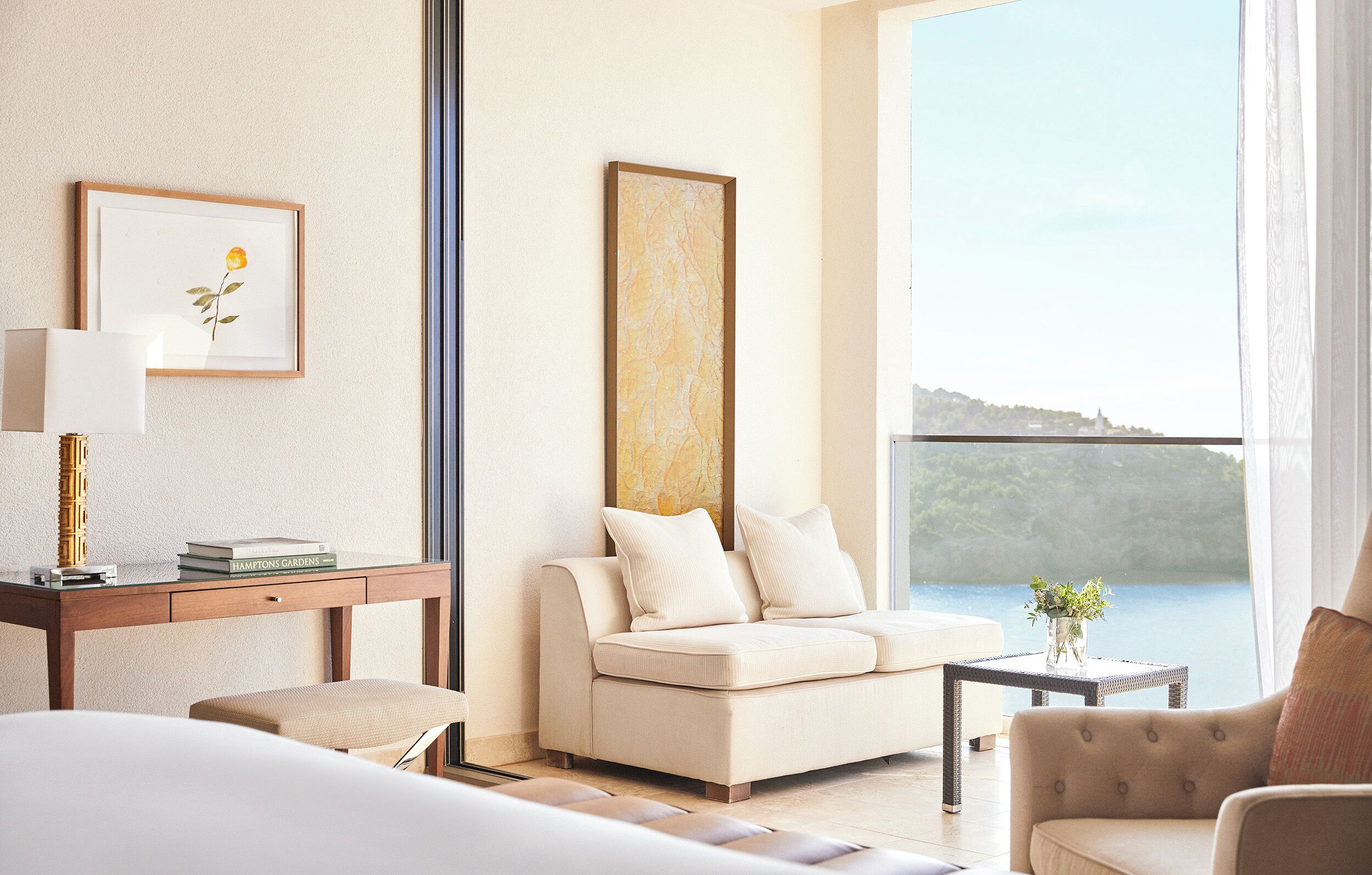 Una habitación de hotel moderna con un ventanal grande, un sofá, un escritorio con lámpara y un cuadro en la pared.