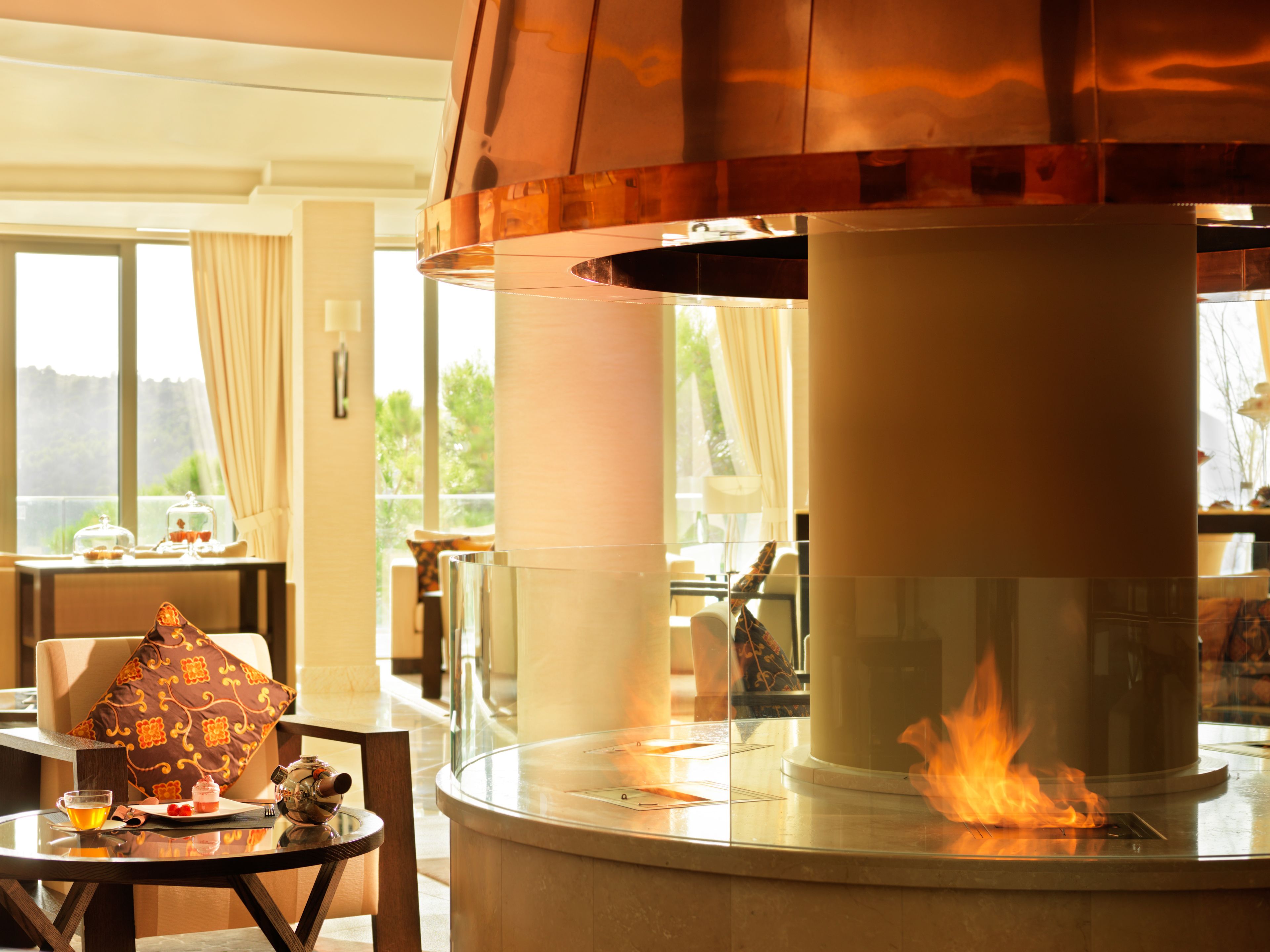A modern interior with a central fireplace, a dining area with a table and chairs, and a view through large windows.