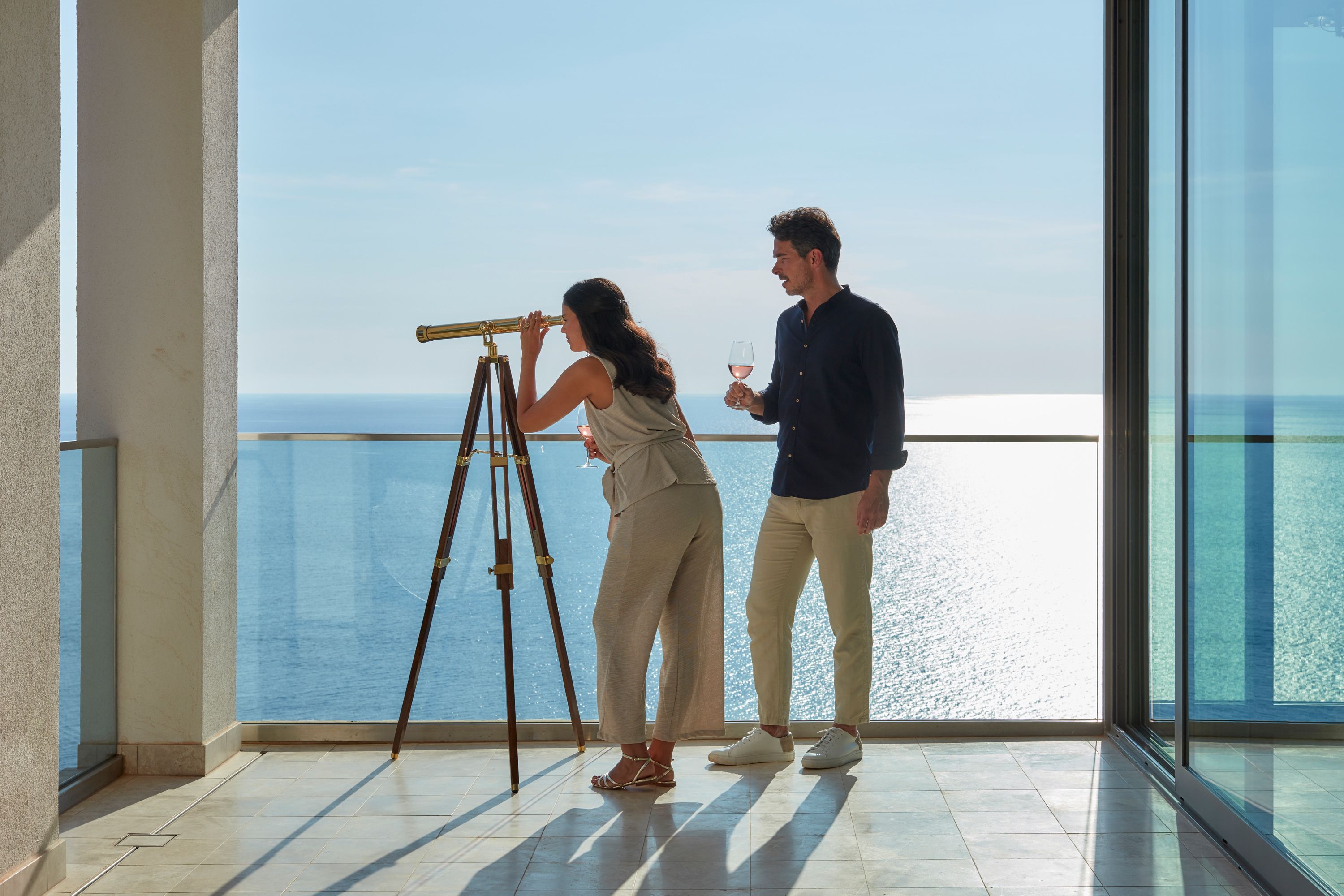 Una pareja de pie junto a un balcón con vistas despejadas al mar.
