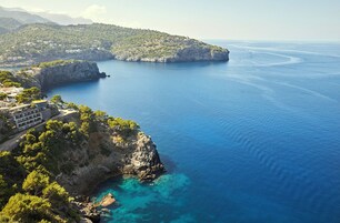 A coastal property with a rocky cliff, clear blue waters, and a view of the sea.