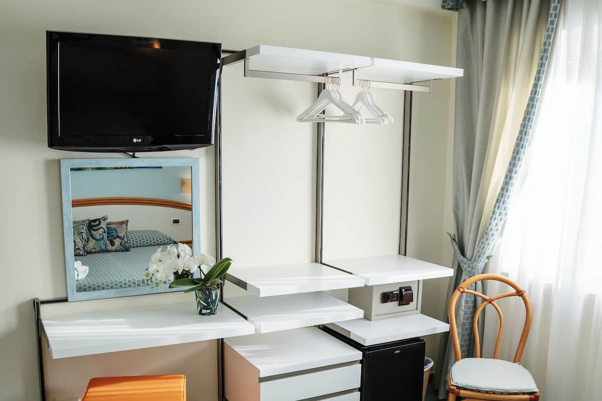 A hotel room with a bed, a desk with a chair, a television, a mirror, and a window with curtains.