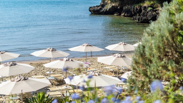 Una playa con sombrillas y sillas de descanso, un bote en el agua y un acantilado rocoso con vegetación.