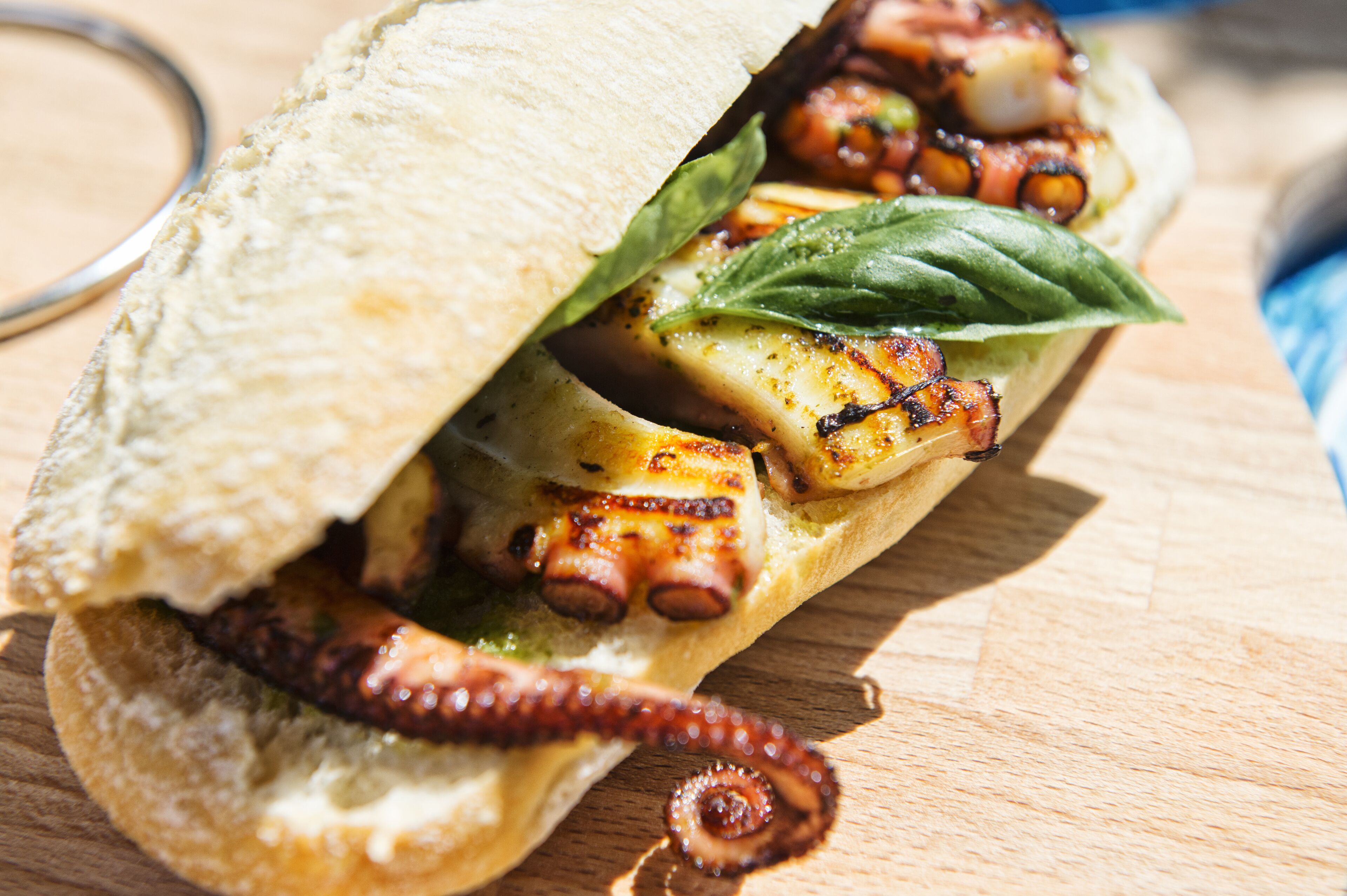 A sandwich with grilled octopus and vegetables on a wooden surface.