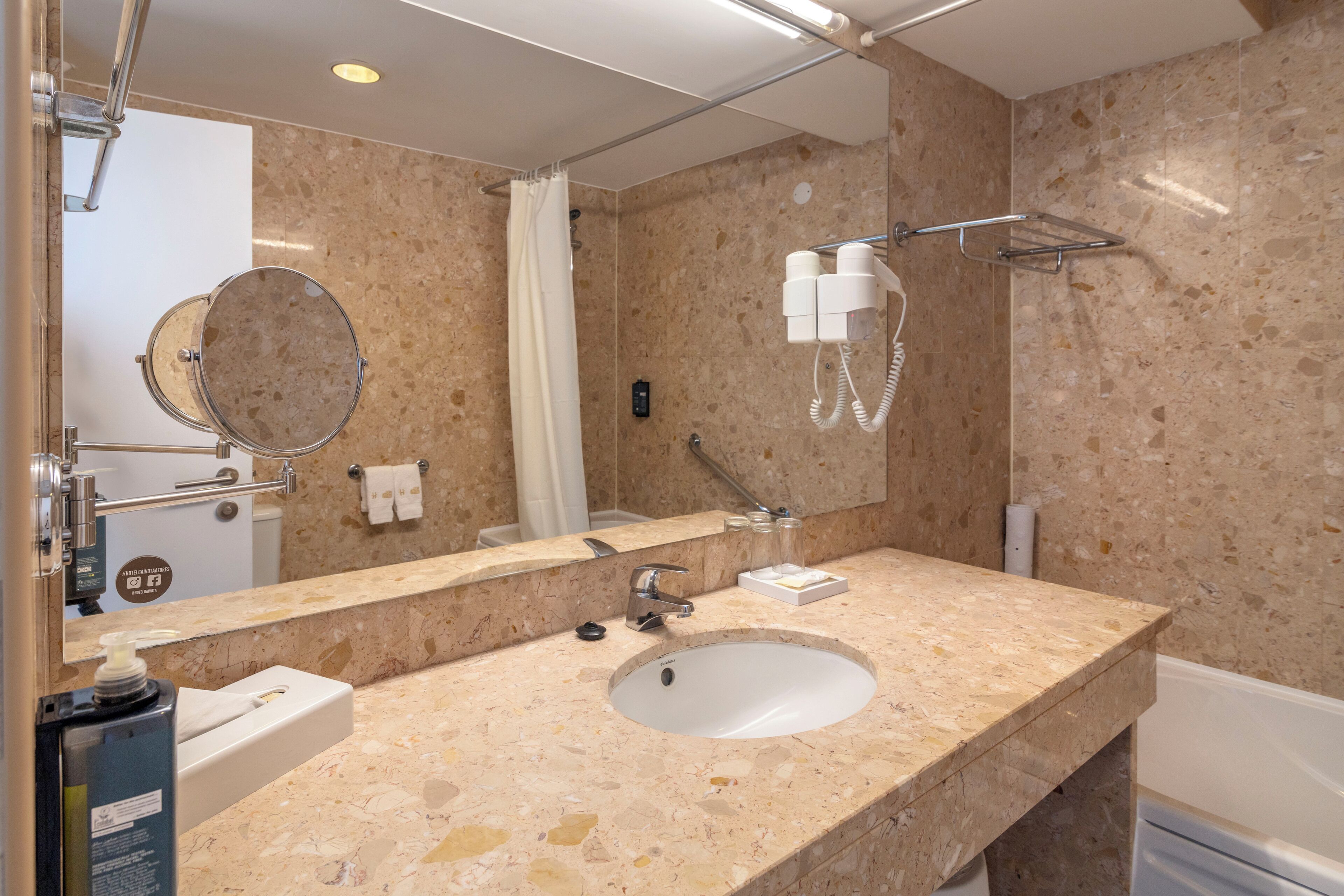 A bathroom with a marble sink, a mirror, a towel rack, a shower, and a hairdryer.