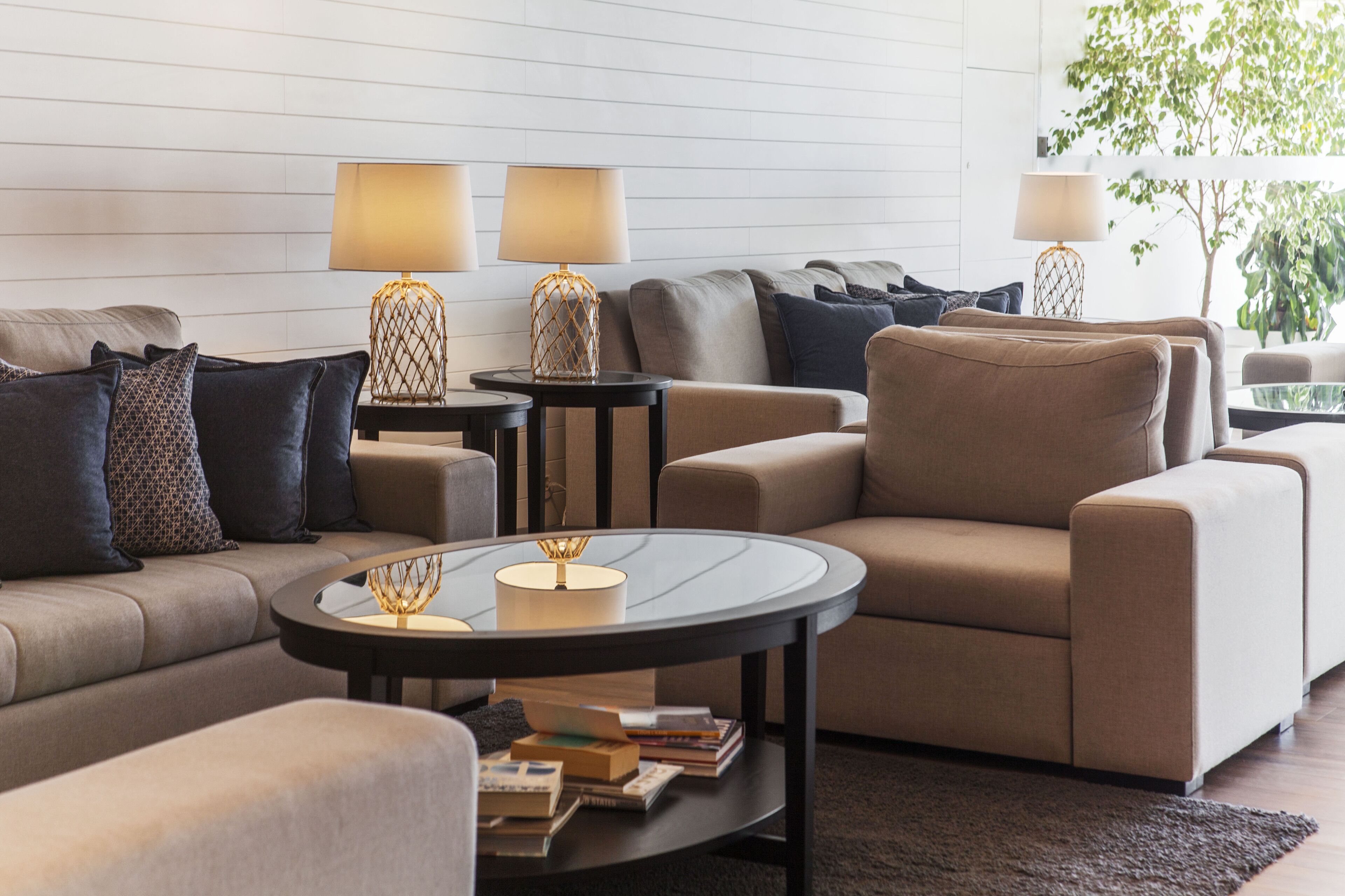 Un salon moderne avec un canapé beige, deux tables d’appoint avec des lampes et une table basse sur laquelle sont posés des livres.