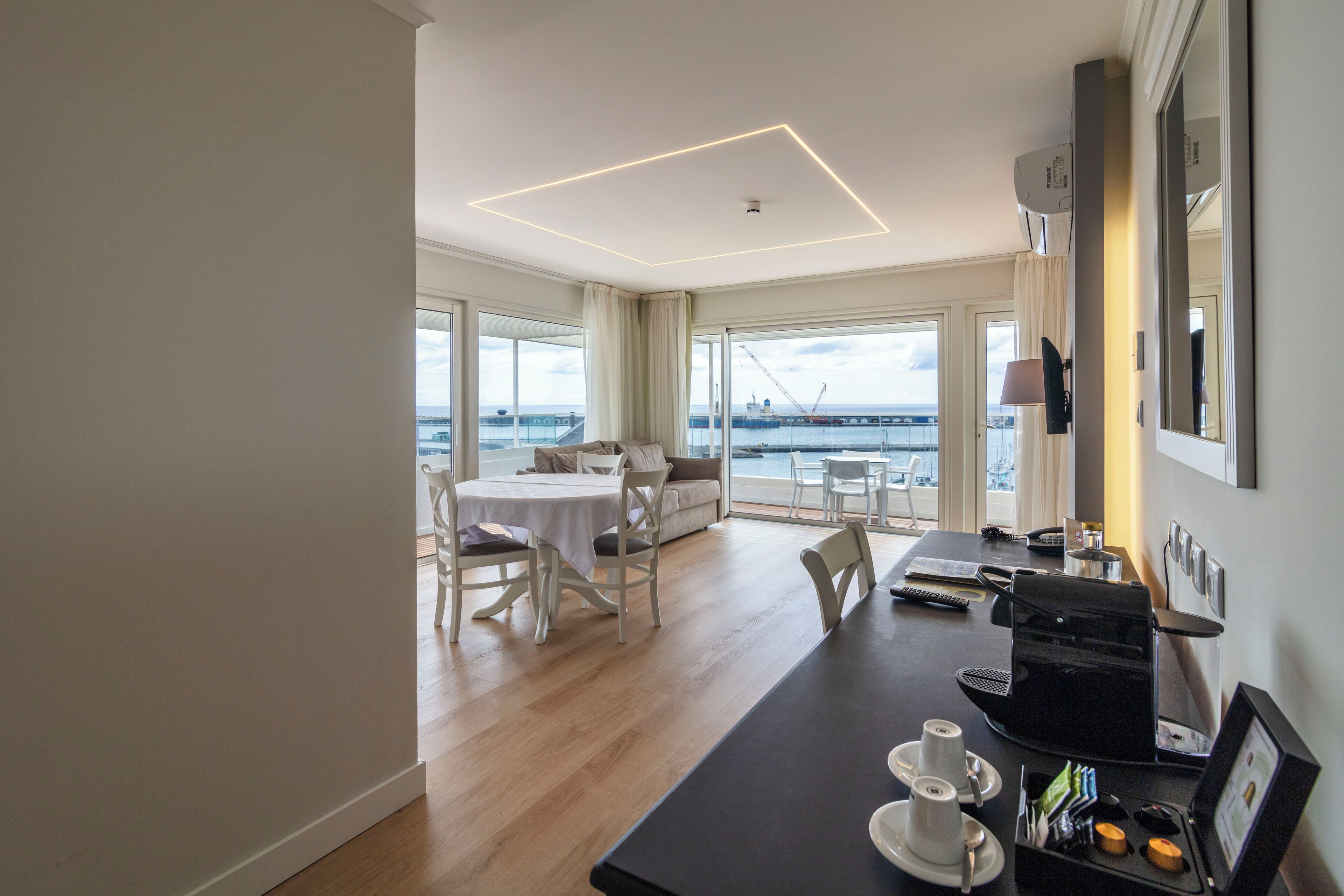 Een moderne hotelkamer met een zithoek, grote ramen met uitzicht op zee, en een flatscreen-televisie.