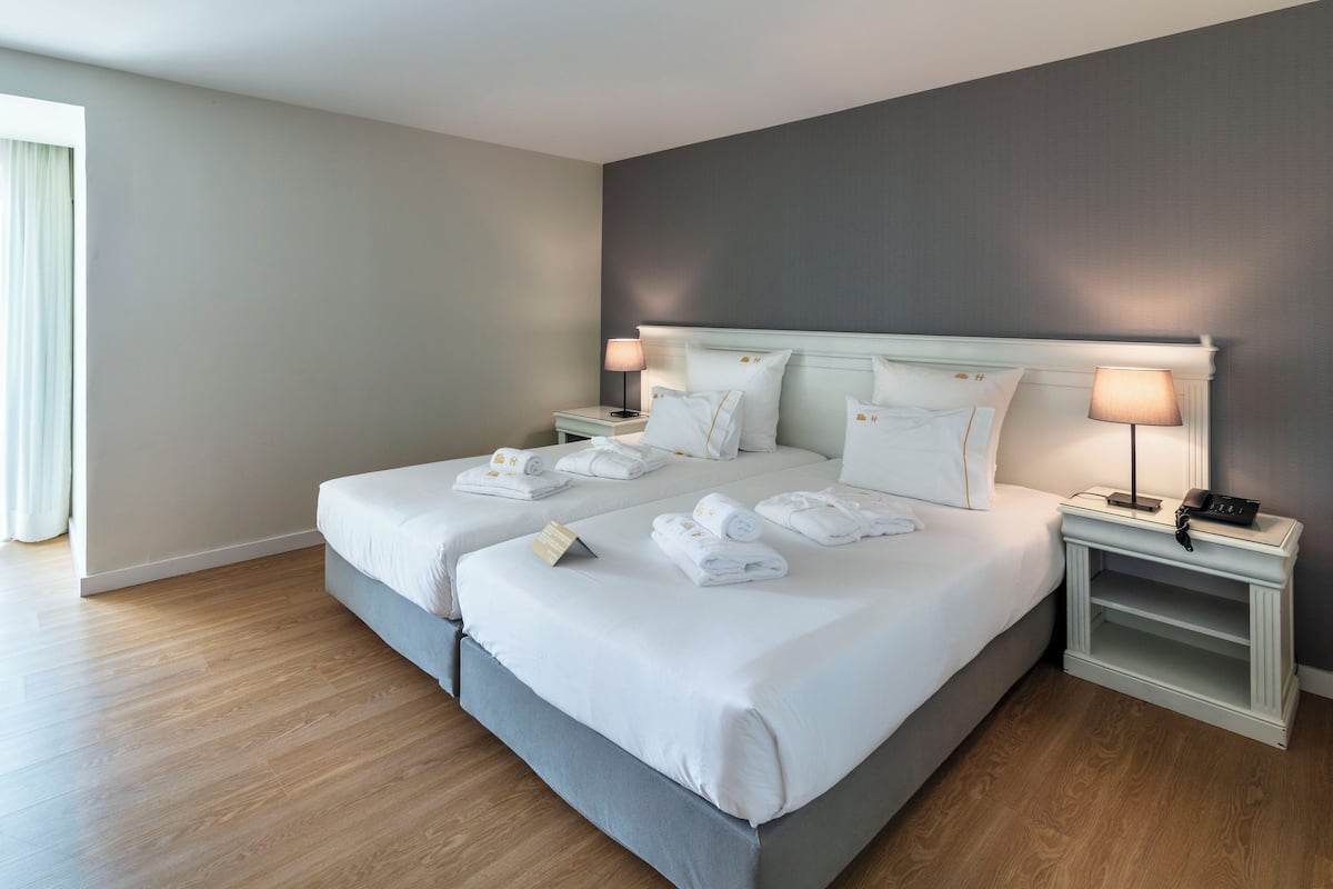 A double bed with white linens and towels, bedside tables with lamps, and a view of the room's wooden floor and walls.