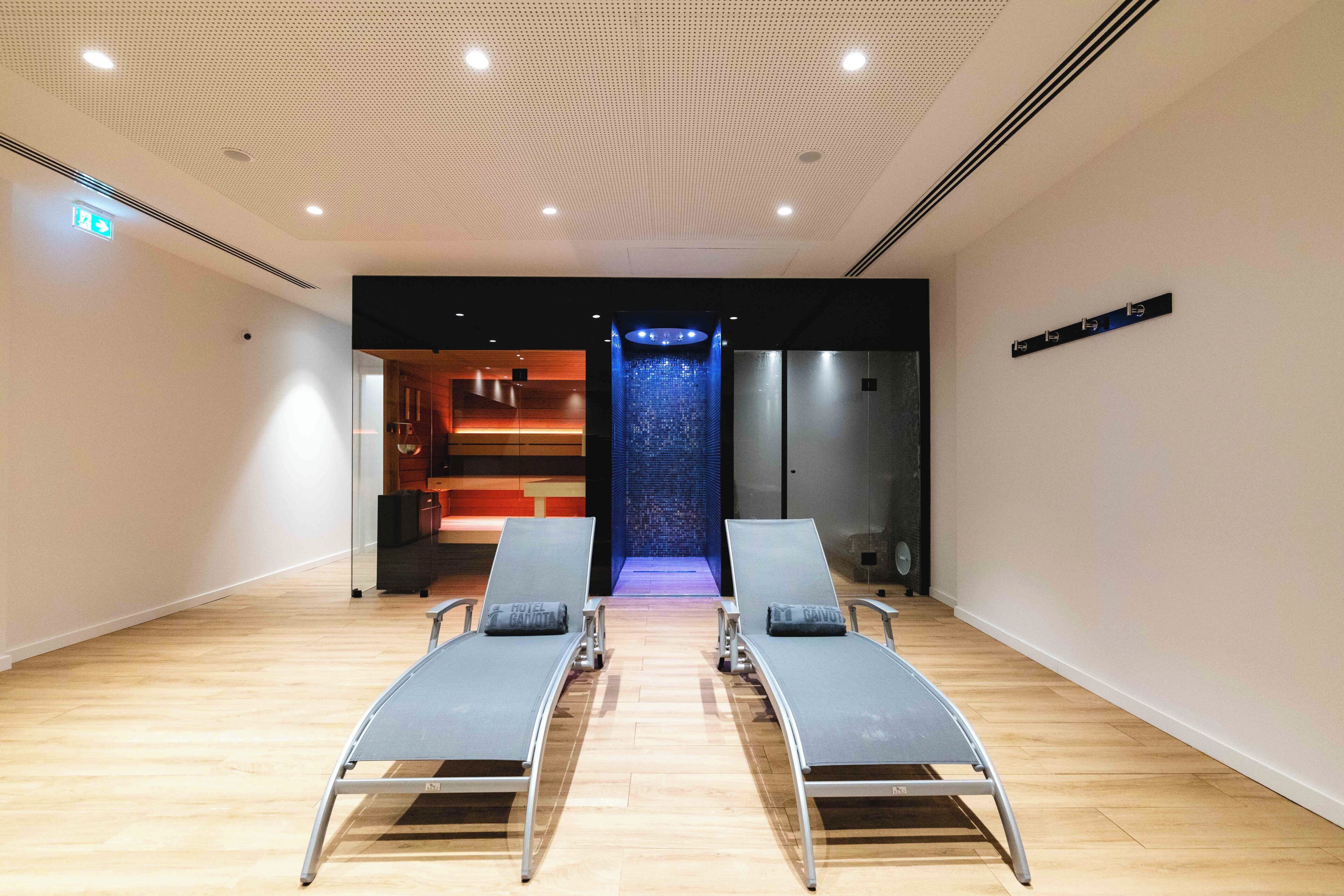 Un moderno spa con dos sillones de descanso, una fuente de agua azul y una recepción al fondo.