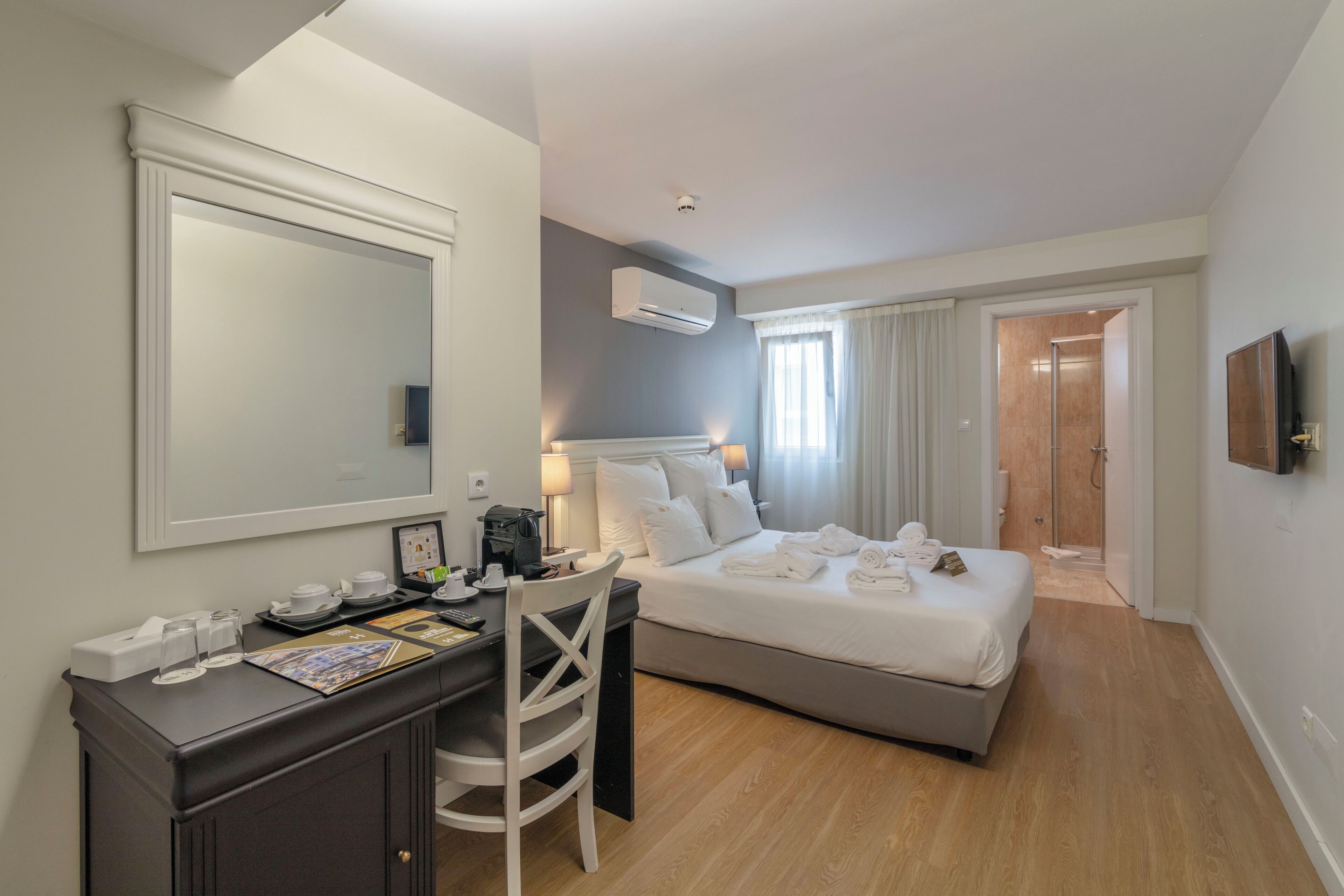 Habitación de hotel con cama, escritorio con silla, espejo, televisión y aire acondicionado.