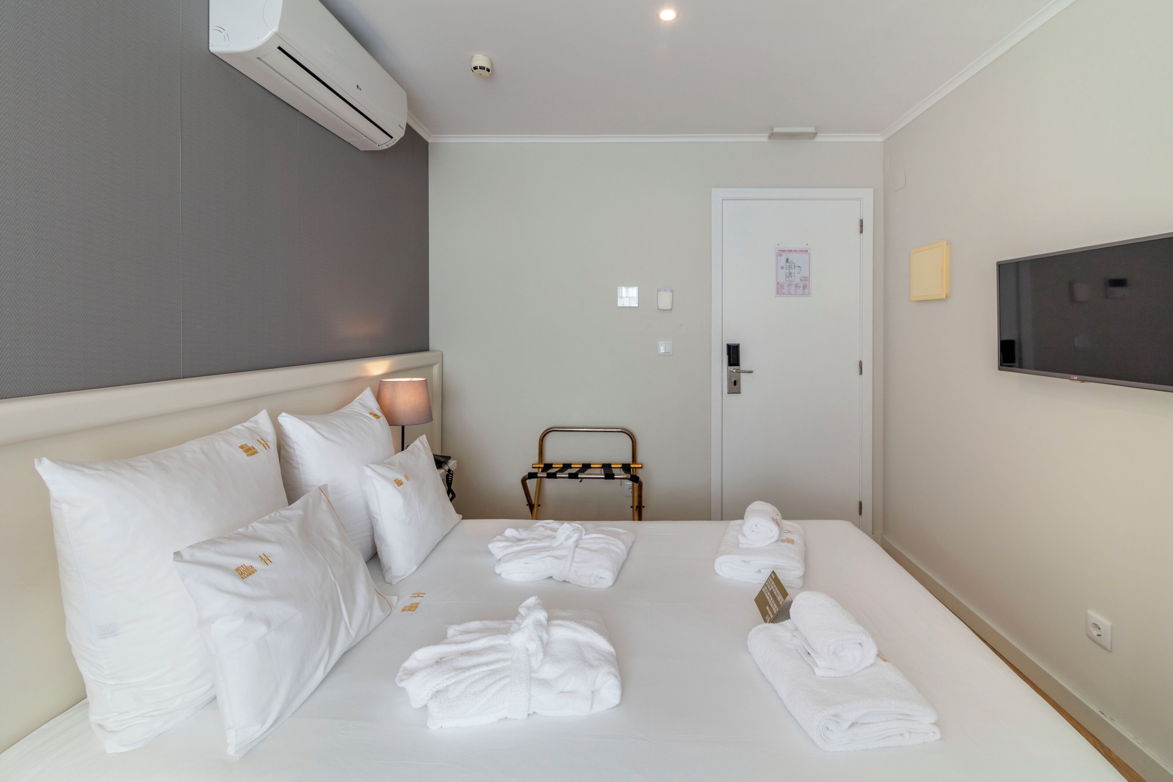 Una habitación de hotel con una cama, almohadas blancas, un televisor, una silla y toallas.