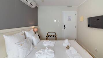 Habitació d'hotel amb un llit, almoinades blanques, un televisor, una cadira i tovalloles.