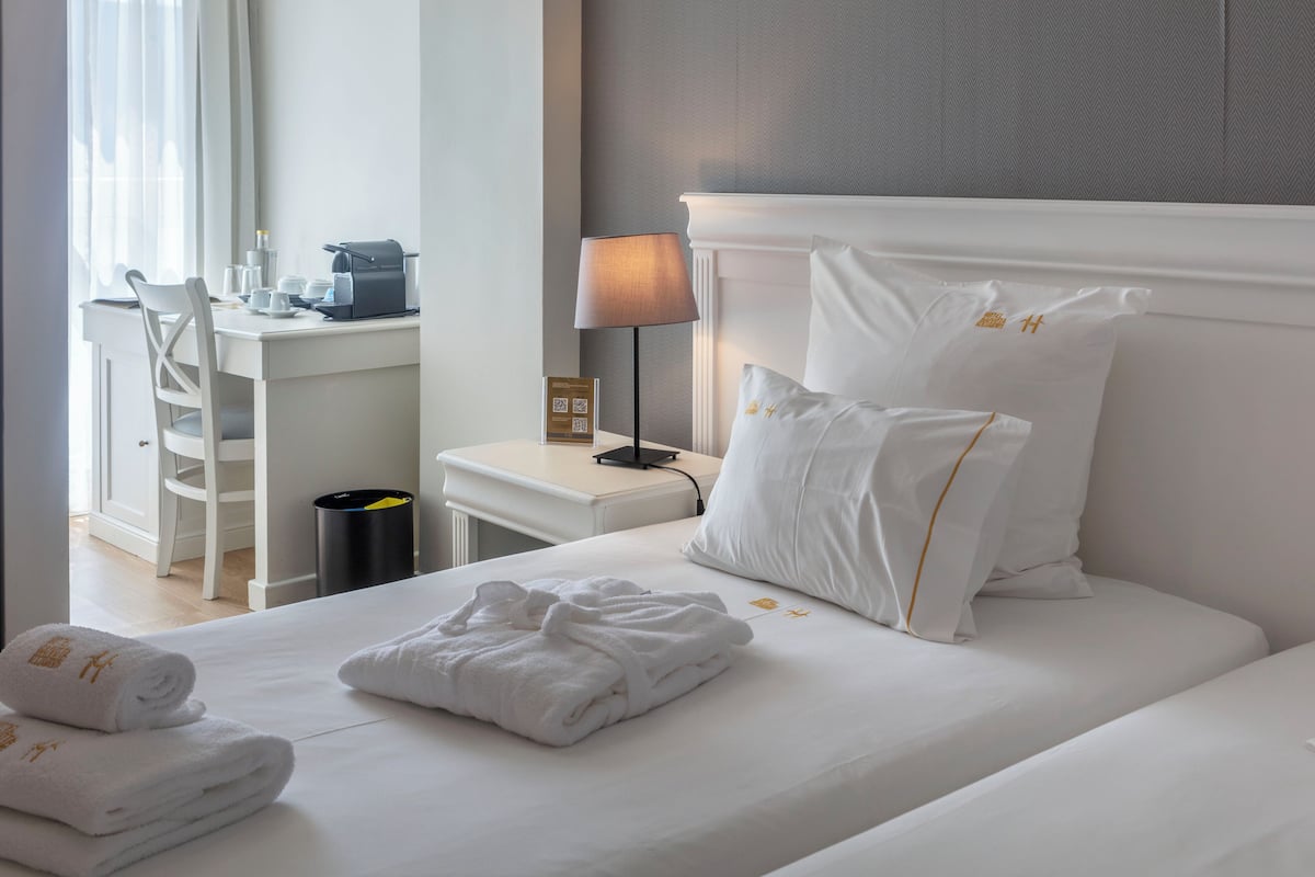 A hotel room with a neatly made bed, a desk with a lamp, and a chair.