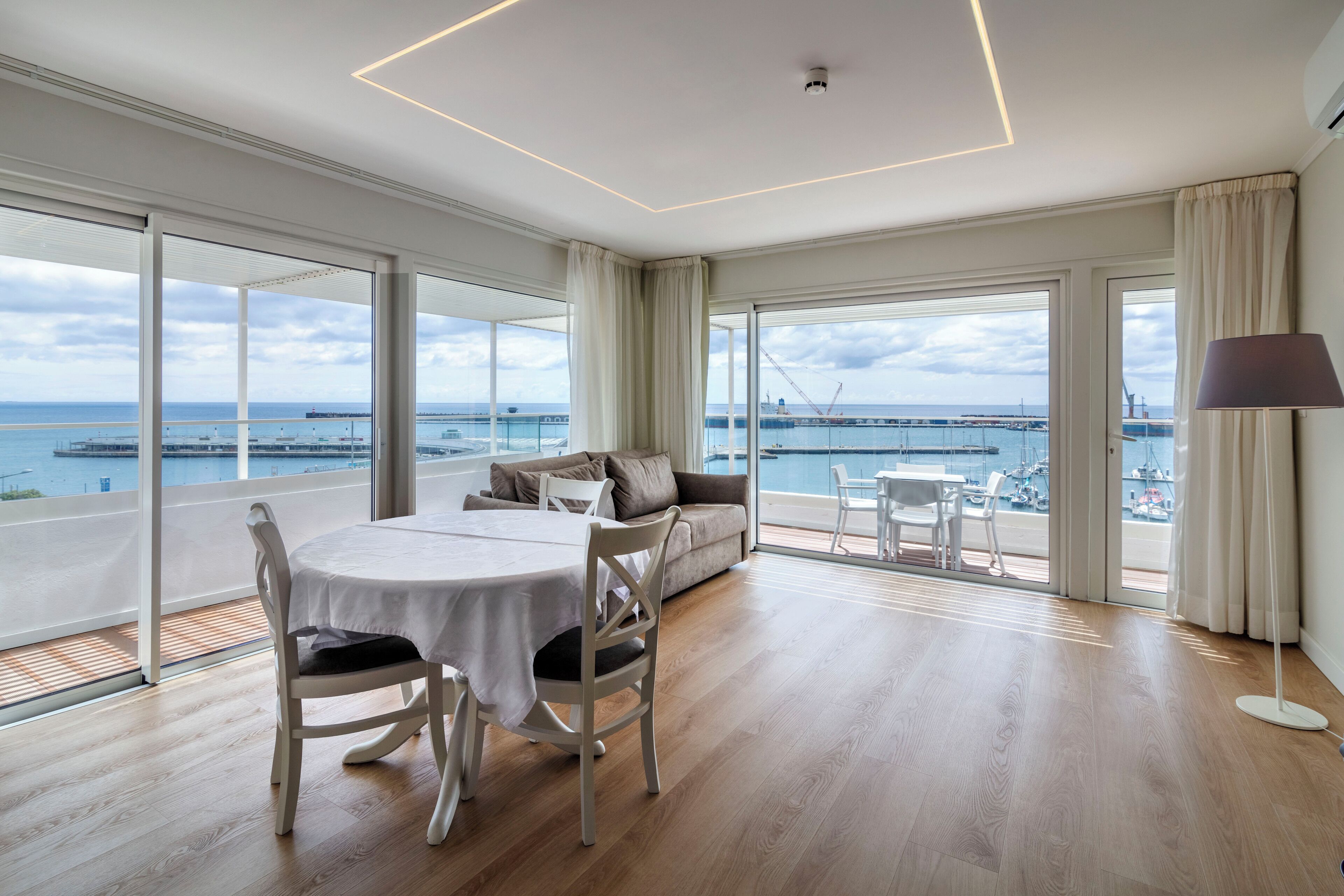 Une pièce spacieuse avec un balcon donnant sur une marina, un coin repas avec une table et des chaises, et un canapé avec vue.