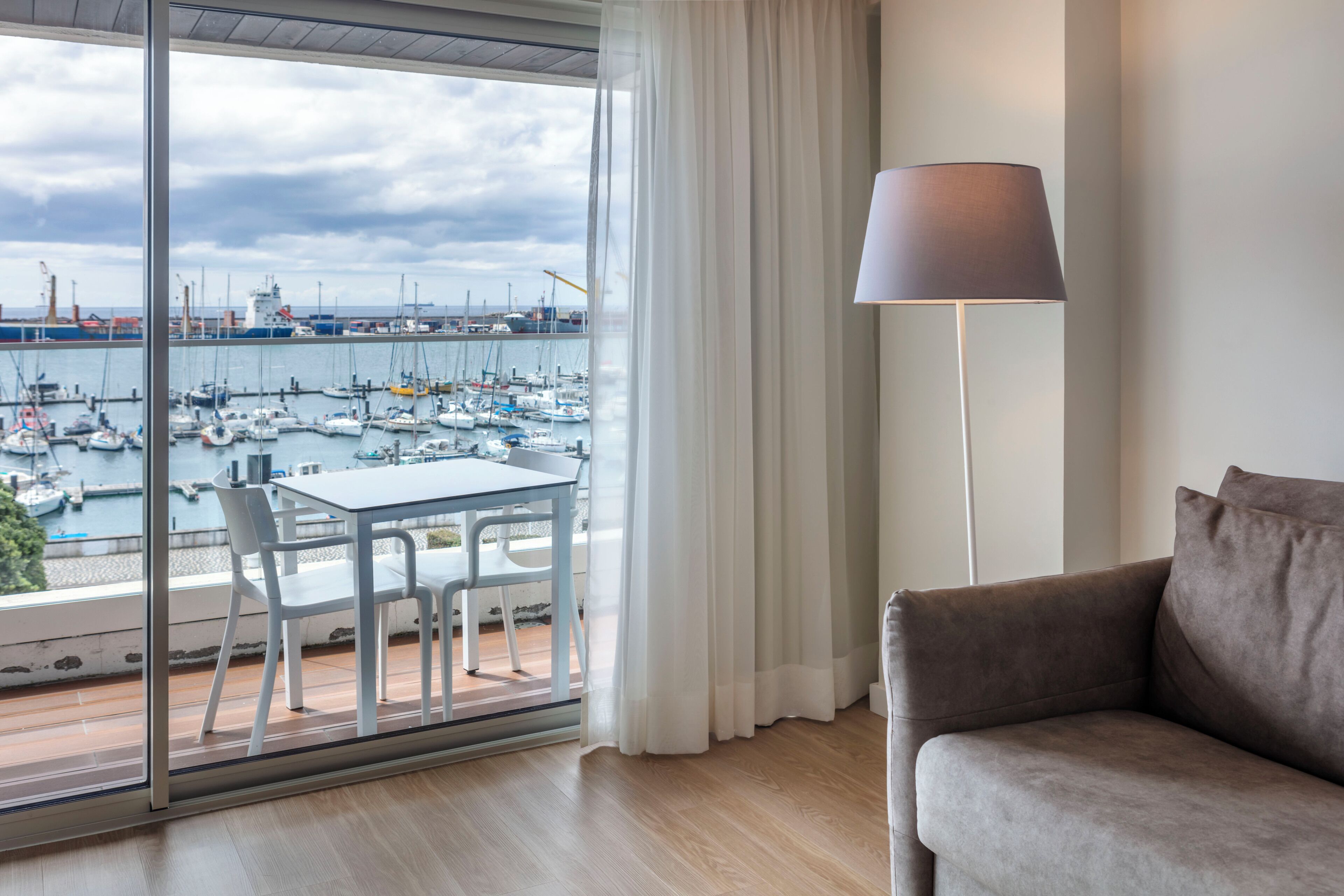 Une pièce avec un balcon donnant sur une marina, une table avec des chaises, une lampe et un canapé.
