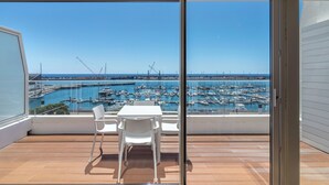 Un balcón con una mesa y sillas, con vistas a un puerto deportivo con barcos y grúas.
