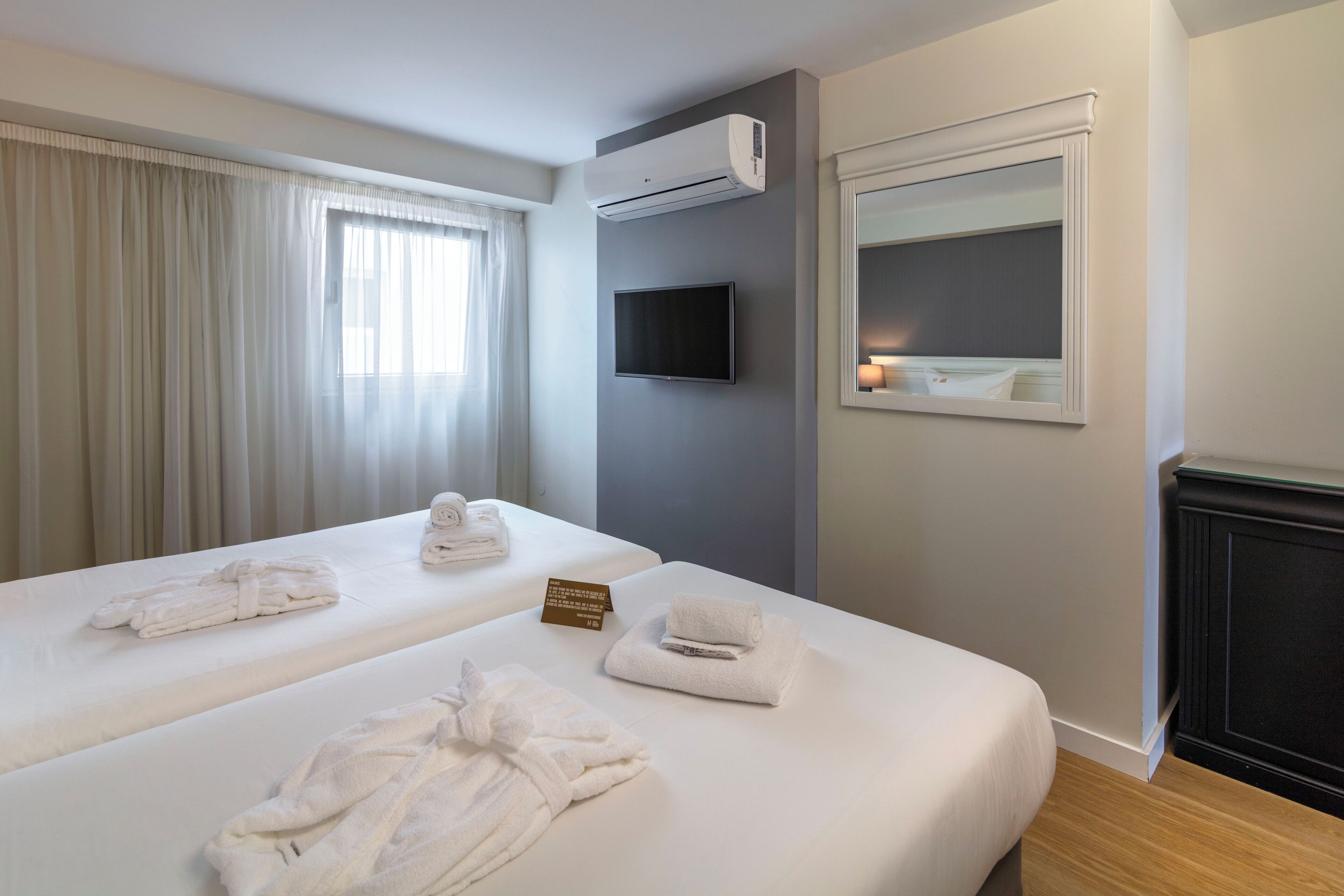Two beds with towels, a flat-screen TV, an air conditioning unit, a mirror, and a fireplace.