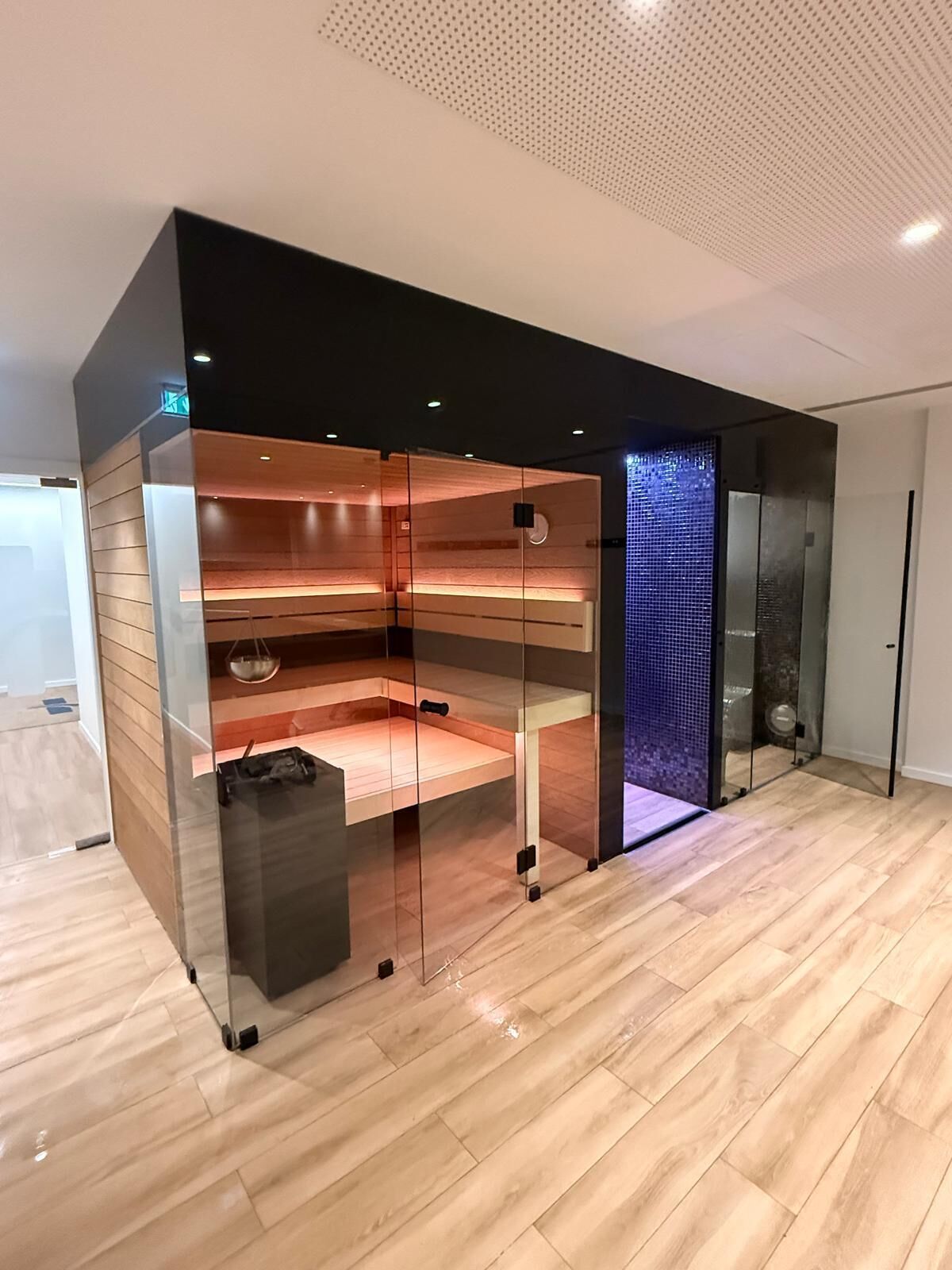 A modern room with a glass partition, wooden flooring, and a blue mosaic wall.