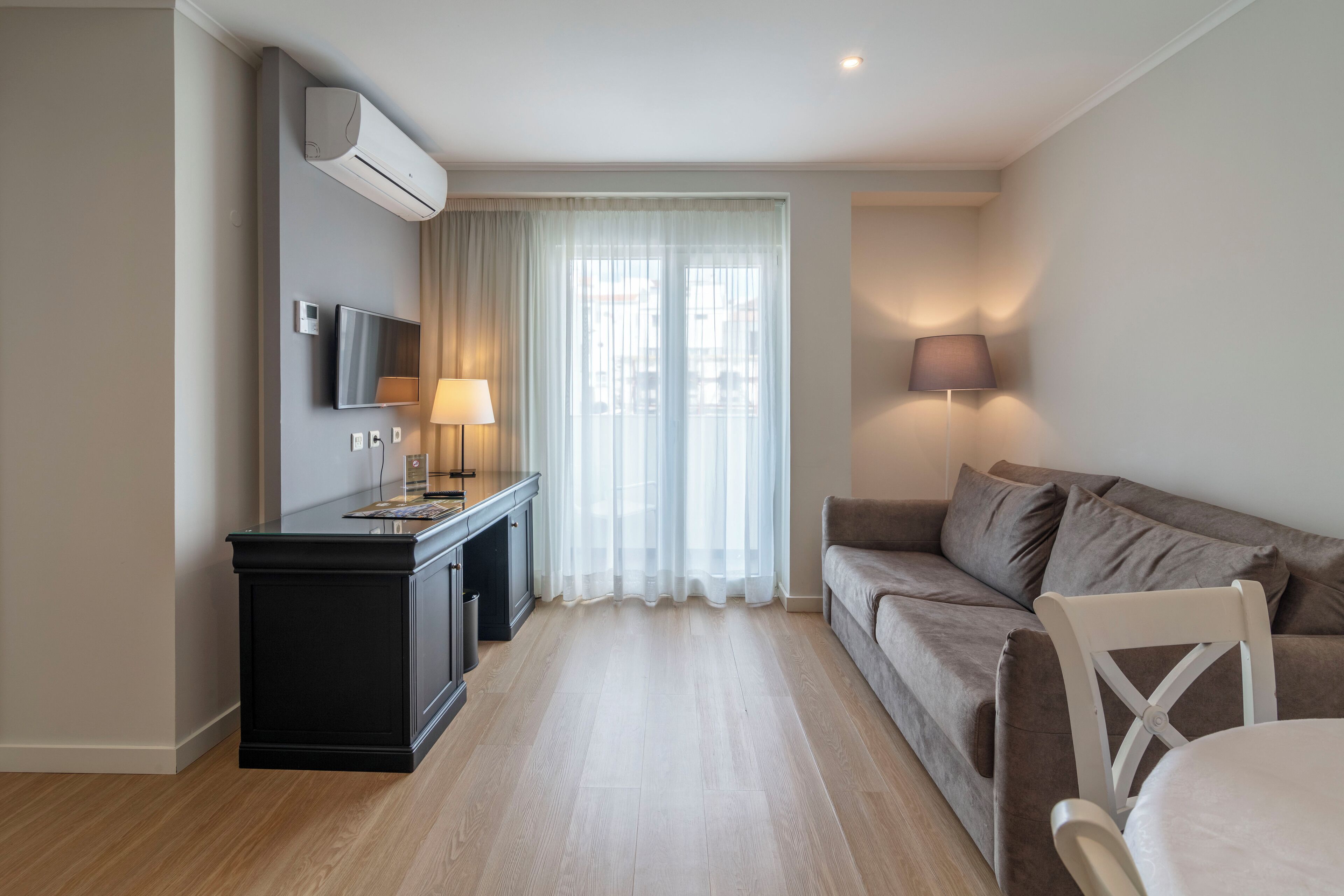 A modern living room with a sofa, a dining table, a TV, and an air conditioning unit.