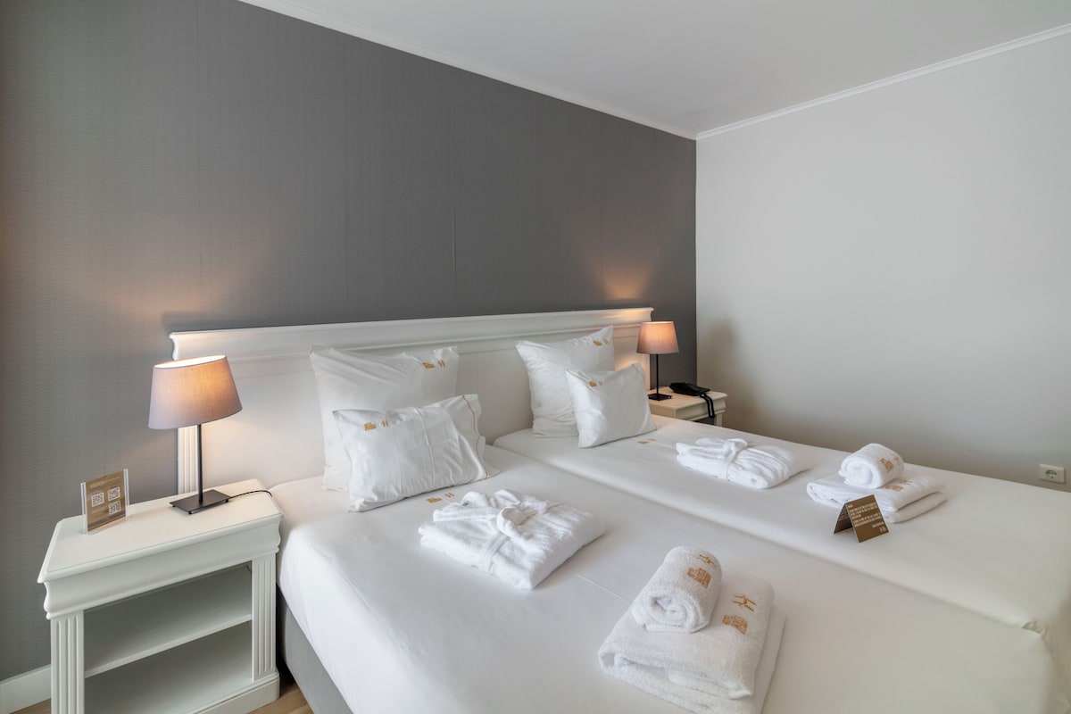 A hotel room with a large bed, two bedside tables, a lamp, and neatly folded towels.