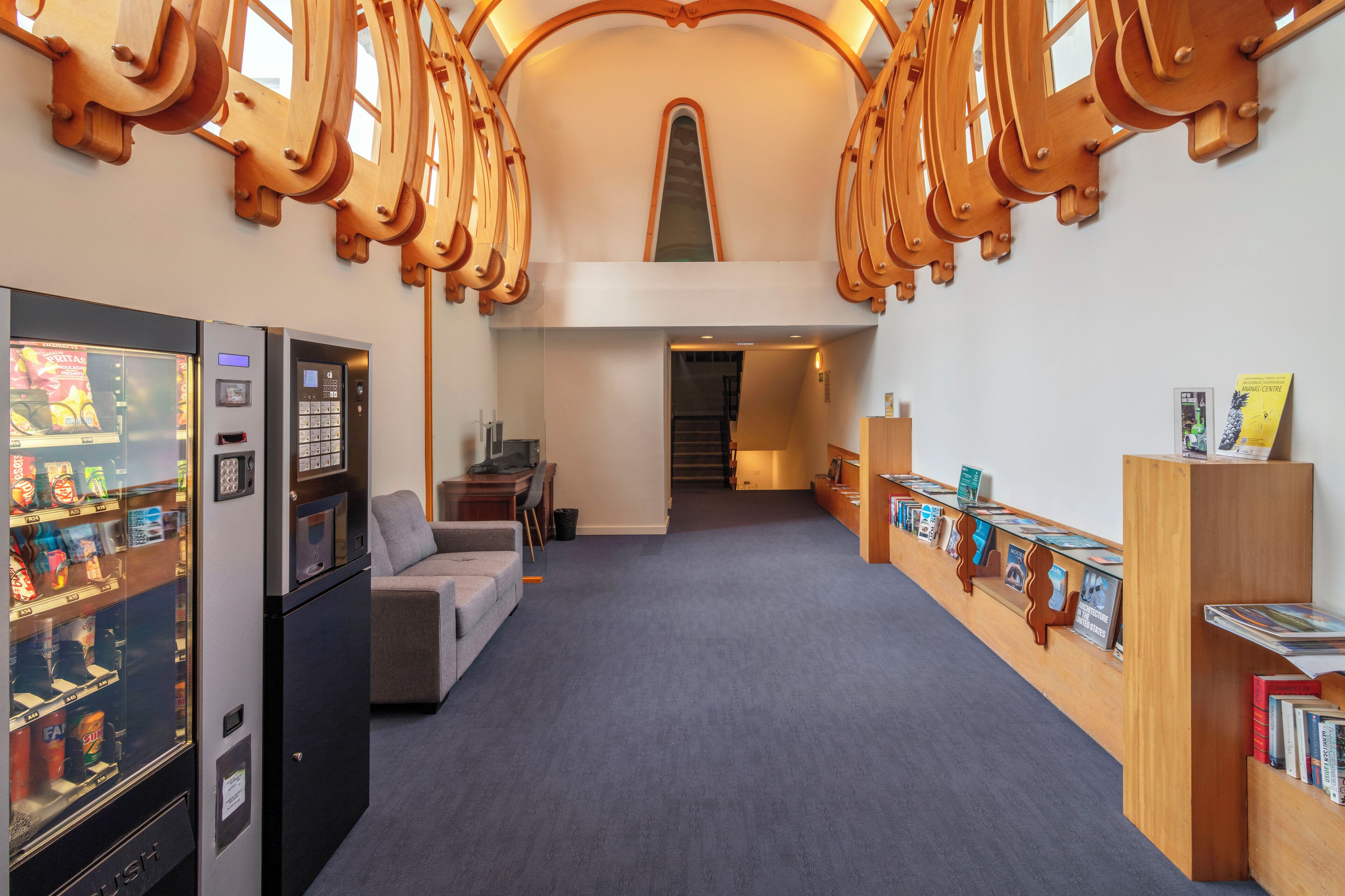 A hotel lobby with a vending machine, a sofa, a staircase, and a bookshelf with books.